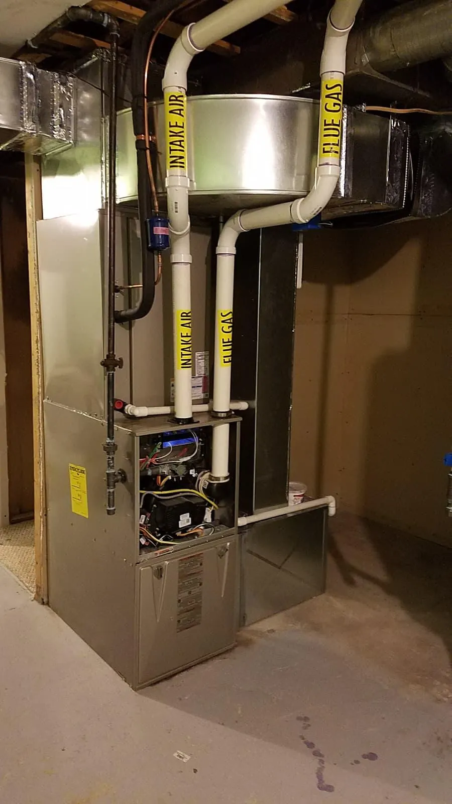 High-efficiency gas furnace installed in a basement utility area with venting pipes and ductwork above it